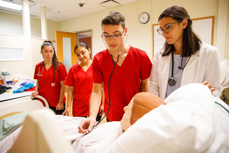 photo of three health sciences students, an instructor and mannequin